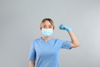 Doctor with protective mask showing muscles on light grey background. Strong immunity concept