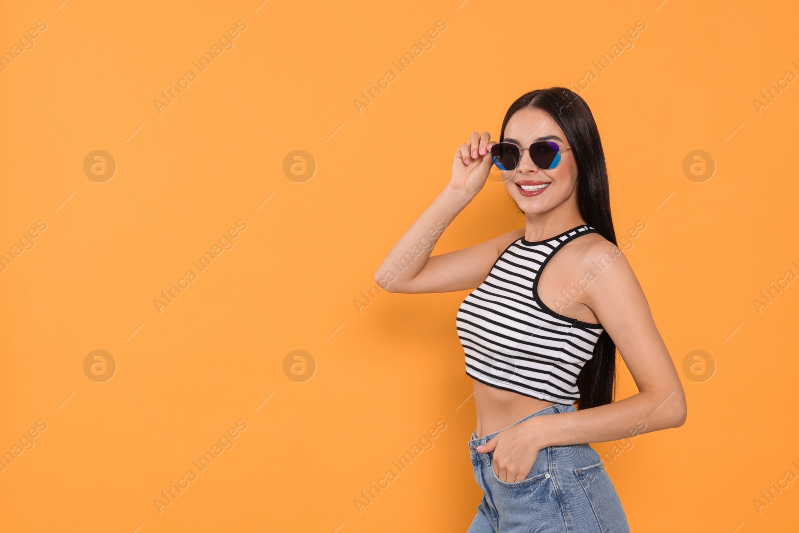 Photo of Attractive happy woman touching fashionable sunglasses against orange background. Space for text