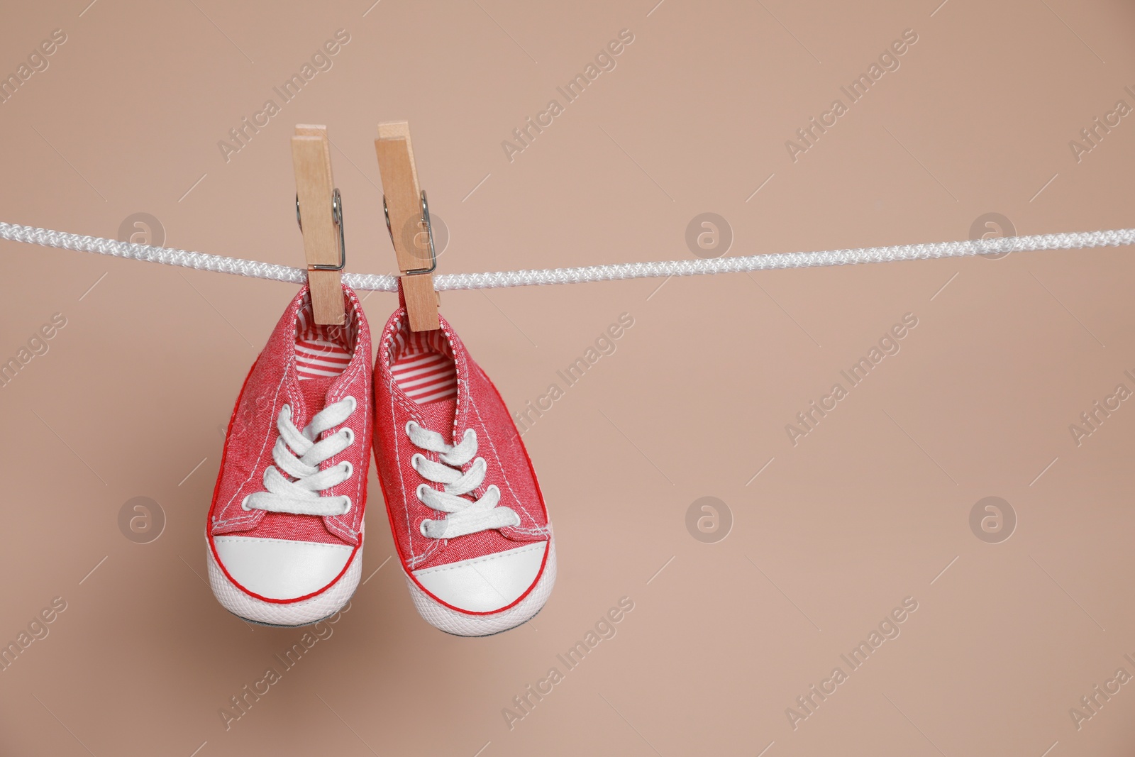 Photo of Cute small baby shoes hanging on washing line against brown background, space for text