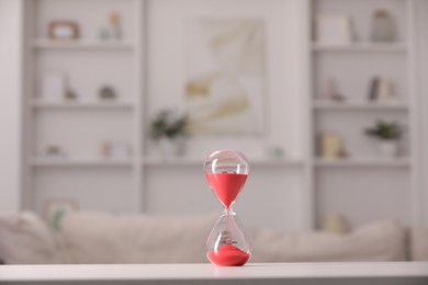 Photo of Hourglass with red flowing sand on white table against blurred background