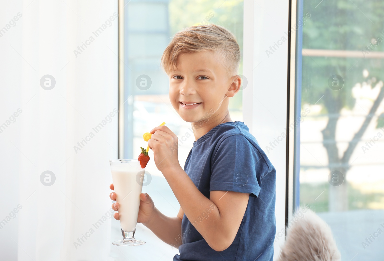 Photo of Little boy with glass of milk shake near window indoors