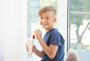 Little boy with glass of milk shake near window indoors