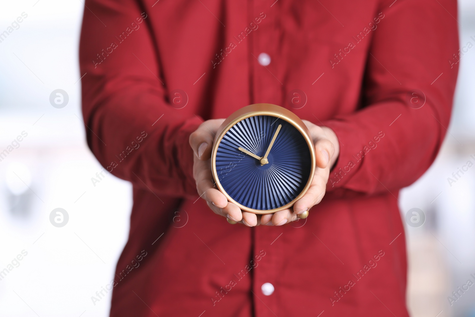 Photo of Young man holding alarm clock on blurred background. Time concept