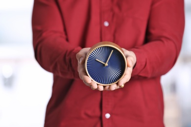 Young man holding alarm clock on blurred background. Time concept