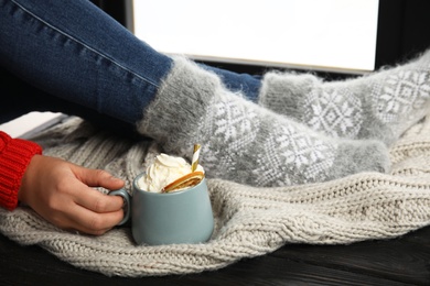 Photo of Woman with cup of hot winter drink with whipped cream sitting on window sill, closeup