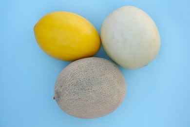 Different tasty ripe melons on light blue background, flat lay