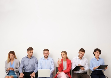 Group of young people waiting for job interview near light wall