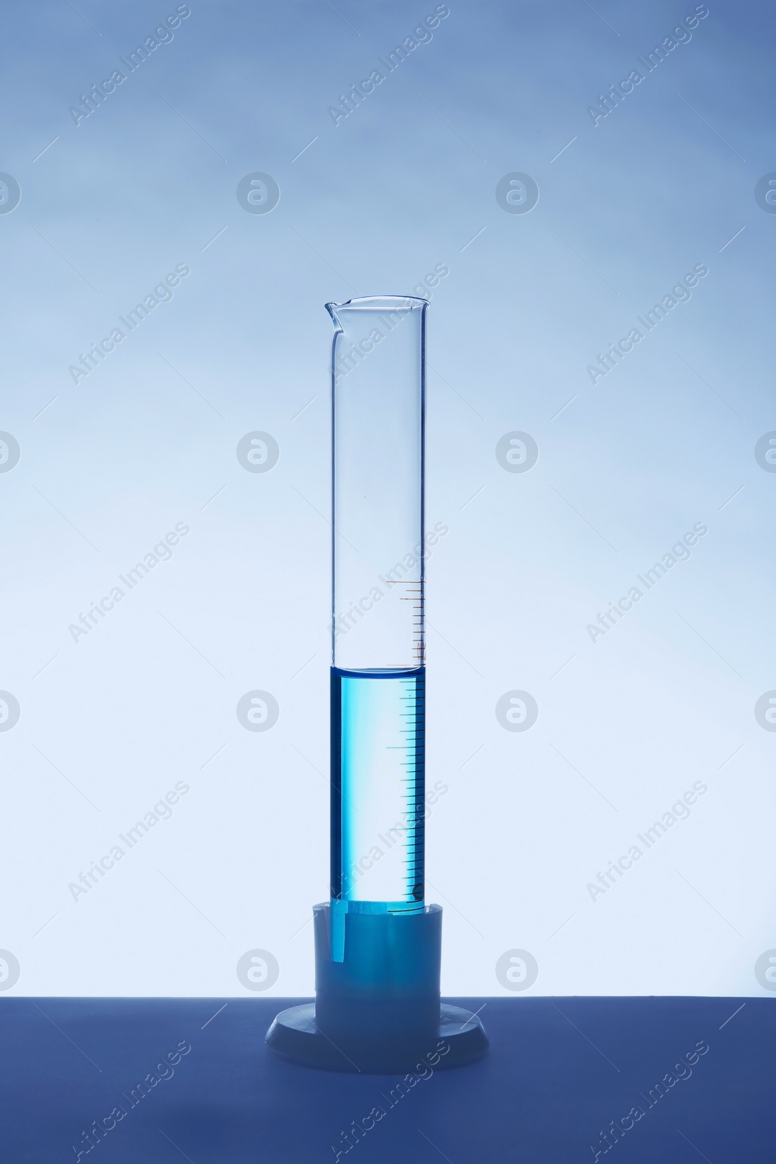 Photo of Graduated cylinder with blue liquid on table against white background. Laboratory analysis