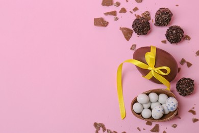 Tasty chocolate eggs and candies on pink background, flat lay. Space for text