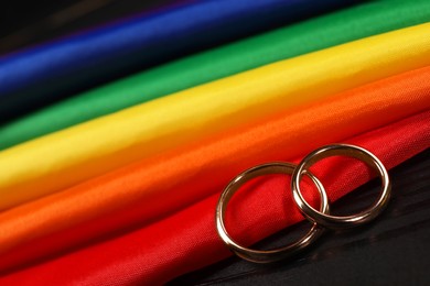 Photo of Rainbow LGBT flag and wedding rings on black wooden background