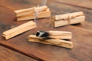 Photo of Palo Santo stick smoldering on wooden table, closeup