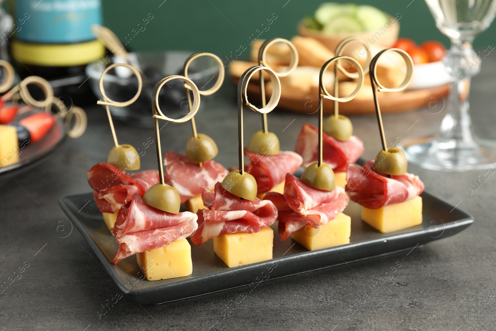 Photo of Tasty canapes with olives, prosciutto and cheese on grey table, closeup