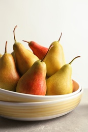 Plate with ripe pears on table against light background