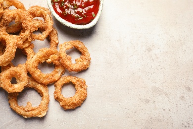 Homemade crunchy fried onion rings and tomato sauce on light background, top view. Space for text