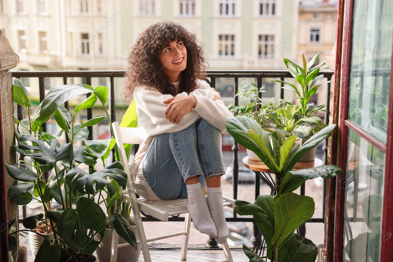 Photo of Beautiful young woman relaxing in chair surrounded by green houseplants on balcony