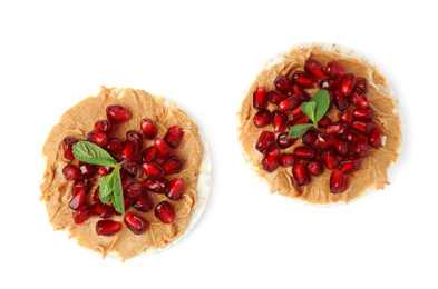 Photo of Puffed rice cakes with peanut butter, pomegranate seeds and mint isolated on white, top view