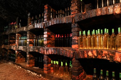 Photo of Many bottles of different alcohol drinks on shelves in cellar