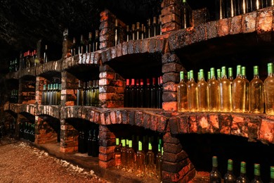 Many bottles of different alcohol drinks on shelves in cellar