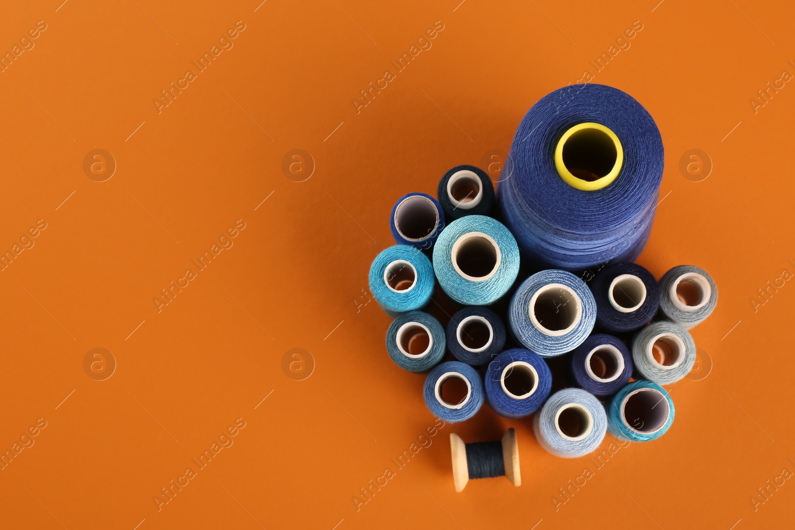 Photo of Different shades of blue sewing threads on orange background, flat lay. Space for text