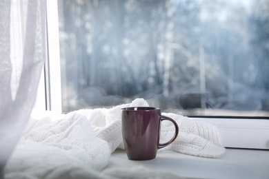 Photo of Cup of winter drink and knitted scarf on windowsill. Space for text