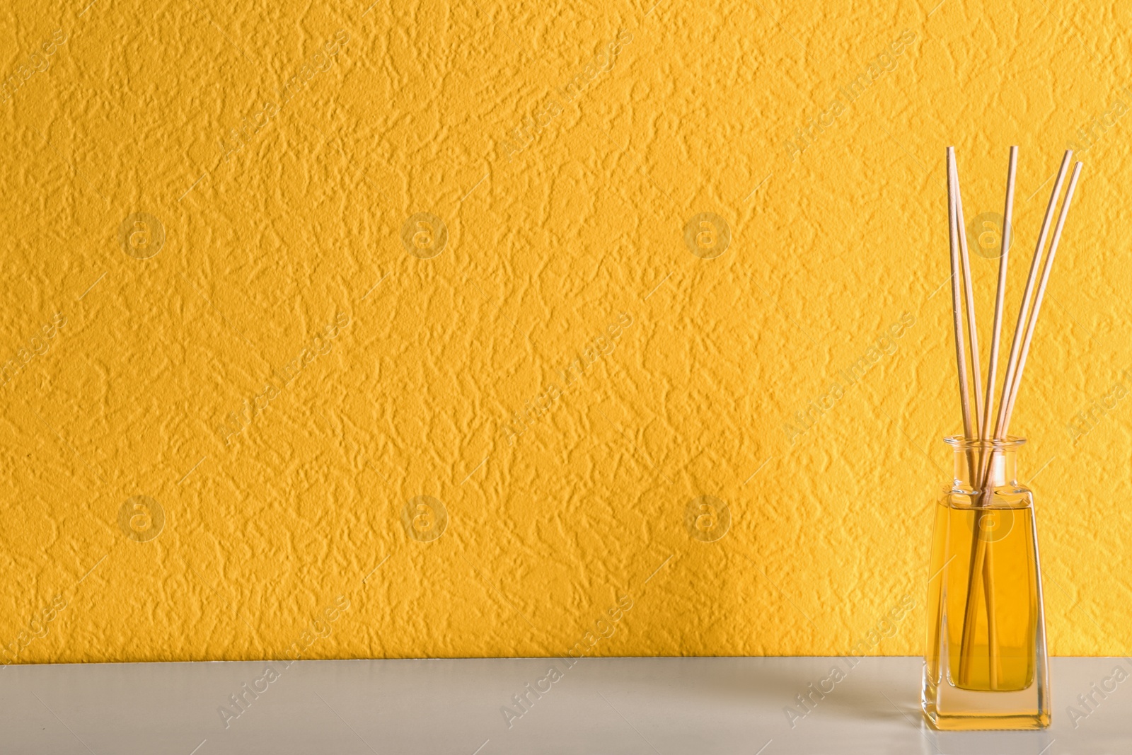 Photo of Reed air freshener on table against orange background, space for text