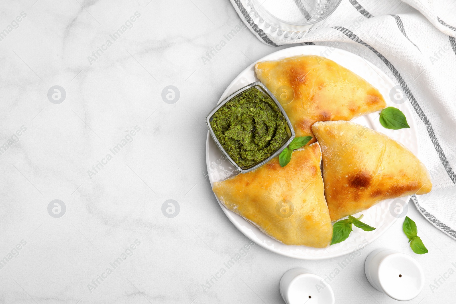 Photo of Delicious samosas with basil and pesto sauce on white marble table, flat lay. Space for text