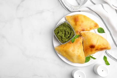 Delicious samosas with basil and pesto sauce on white marble table, flat lay. Space for text