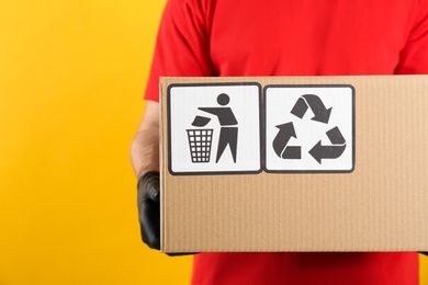 Courier holding cardboard box with different packaging symbols on yellow background, closeup. Parcel delivery
