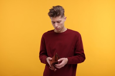 Photo of Upset man looking at his empty wallet on yellow background