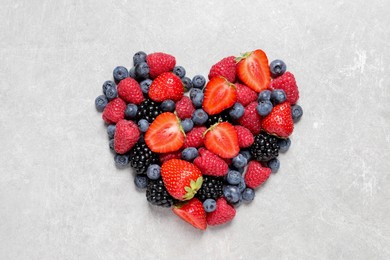 Heart made of different fresh ripe berries on white textured table, top view