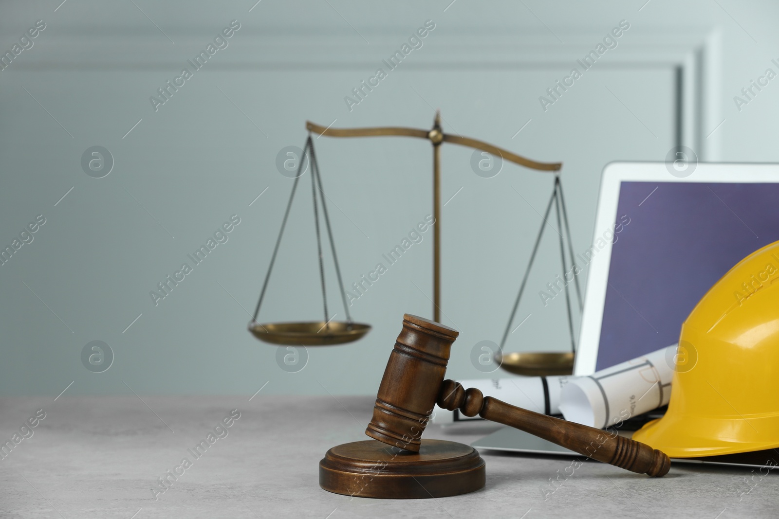 Photo of Construction and land law concepts. Judge gavel, scales of justice, protective helmet, drawings with laptop on light grey table, space for text