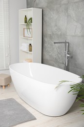 Photo of Stylish bathroom interior with ceramic tub, care products and towels in cabinet