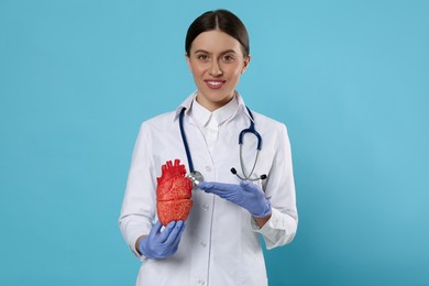 Doctor with stethoscope and model of heart on light blue background. Cardiology concept