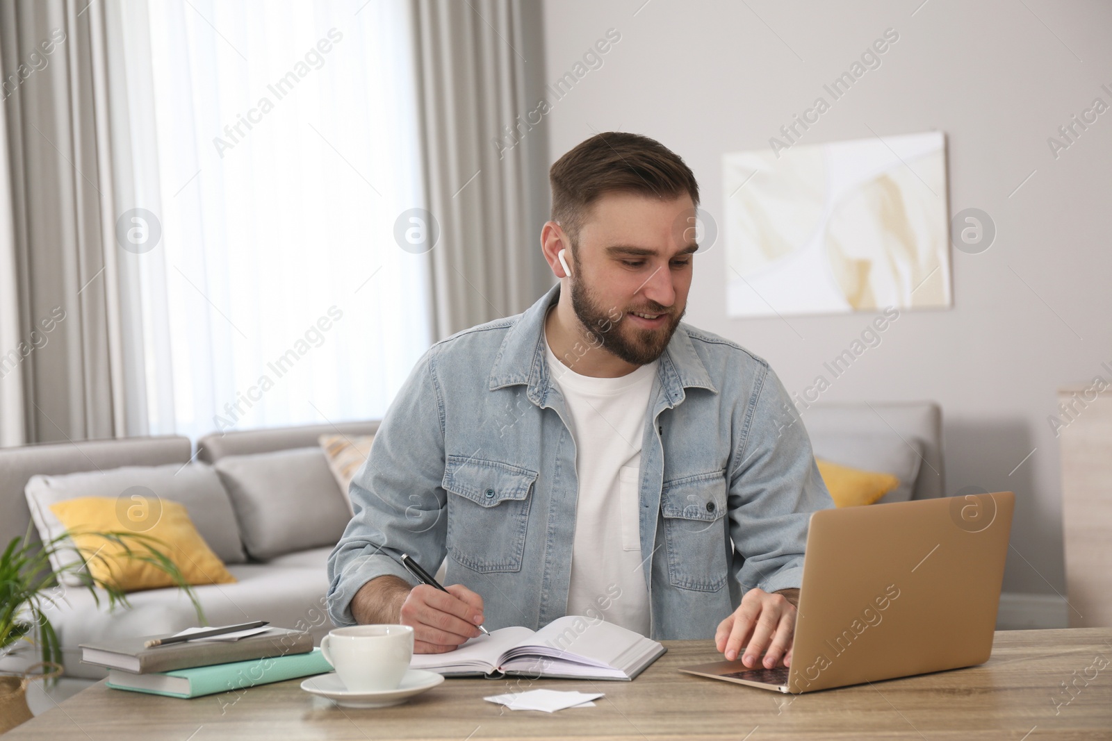 Photo of Young man taking notes during online webinar at table indoors