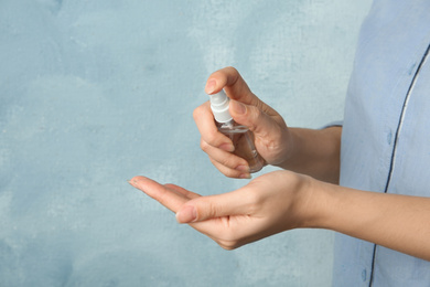 Woman spraying antiseptic onto hand on light blue background, closeup. Virus prevention