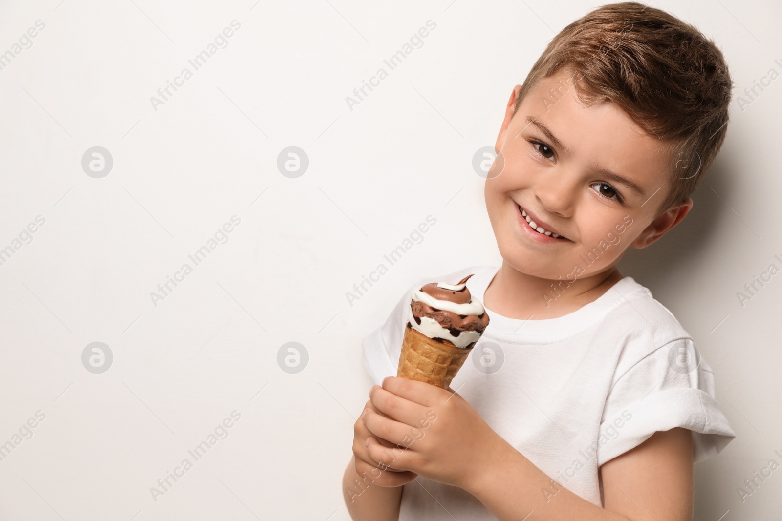 Photo of Cute little boy with delicious ice cream against light background