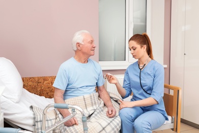 Photo of Nurse measuring senior man's temperature in hospital ward. Medical assisting