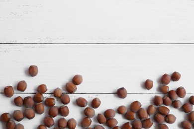 Photo of Tasty hazelnuts on white wooden table, flat lay. Space for text