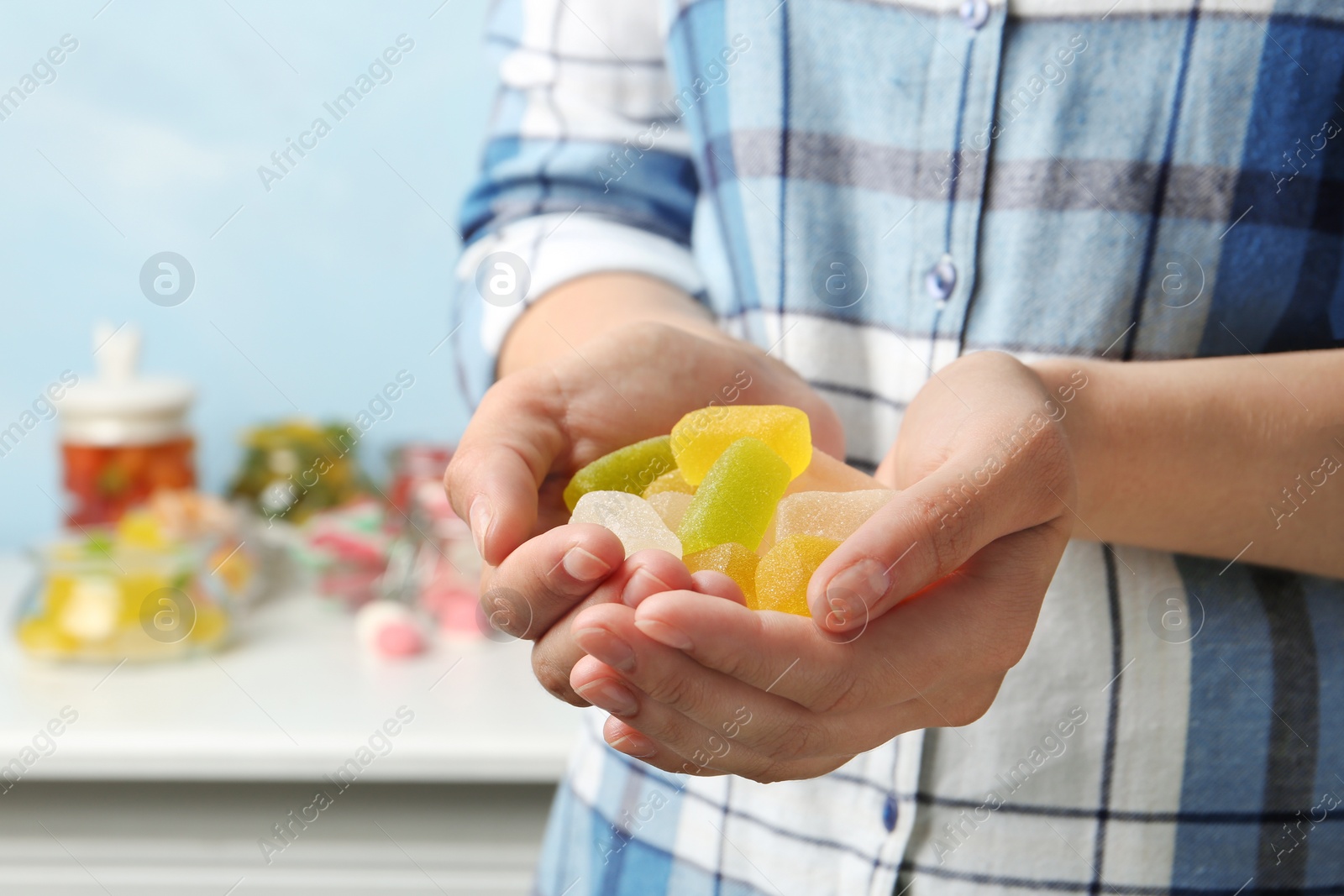 Photo of Young woman holding handful of tasty jelly candies indoors, closeup. Space for text