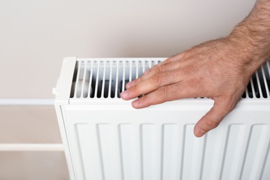 Photo of Man warming hand on heating radiator near color wall