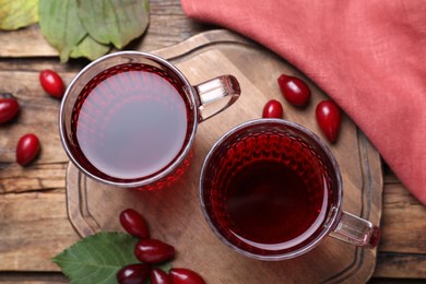 Photo of Glass cups of fresh dogwood tea, berries and leaves on wooden table, flat lay