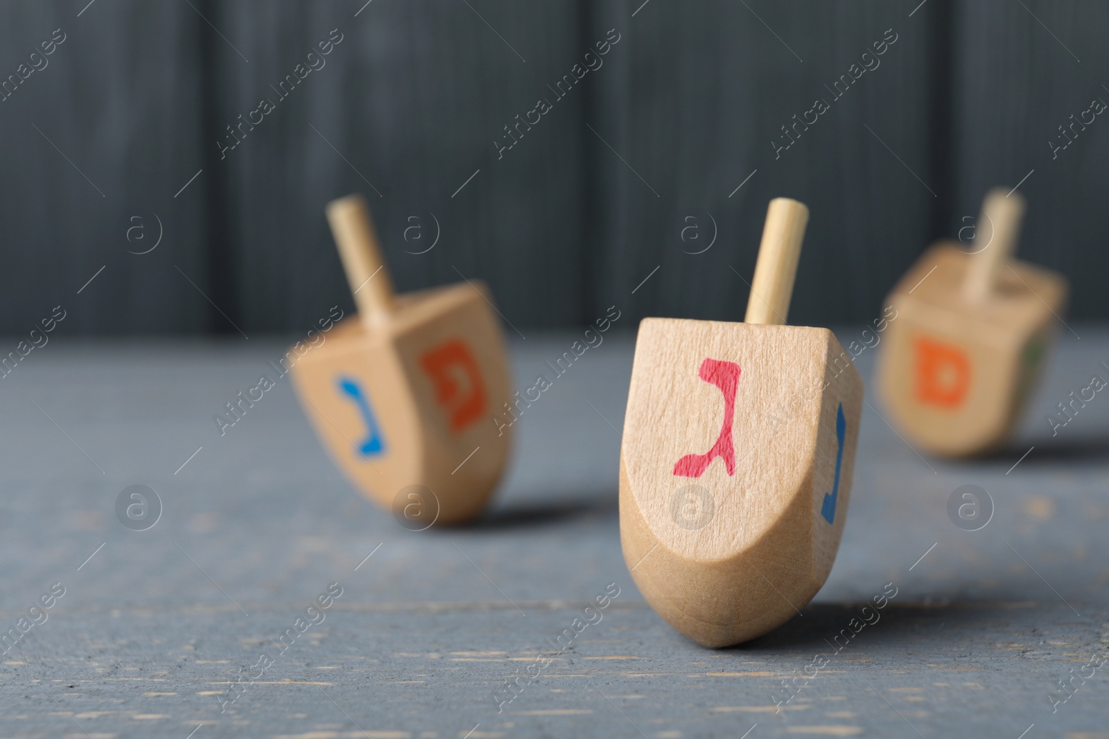 Photo of Hanukkah traditional dreidel with letter Gimel on grey wooden table, closeup. Space for text
