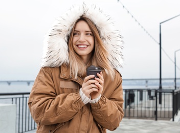 Photo of Young woman with cup of coffee walking outdoors. Space for text