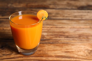 Photo of Glass of tasty carrot juice on wooden table, closeup. Space for text