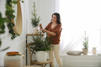 Photo of Woman decorating potted fir tree with Christmas lights at home