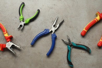 Different pliers on grey textured table, flat lay