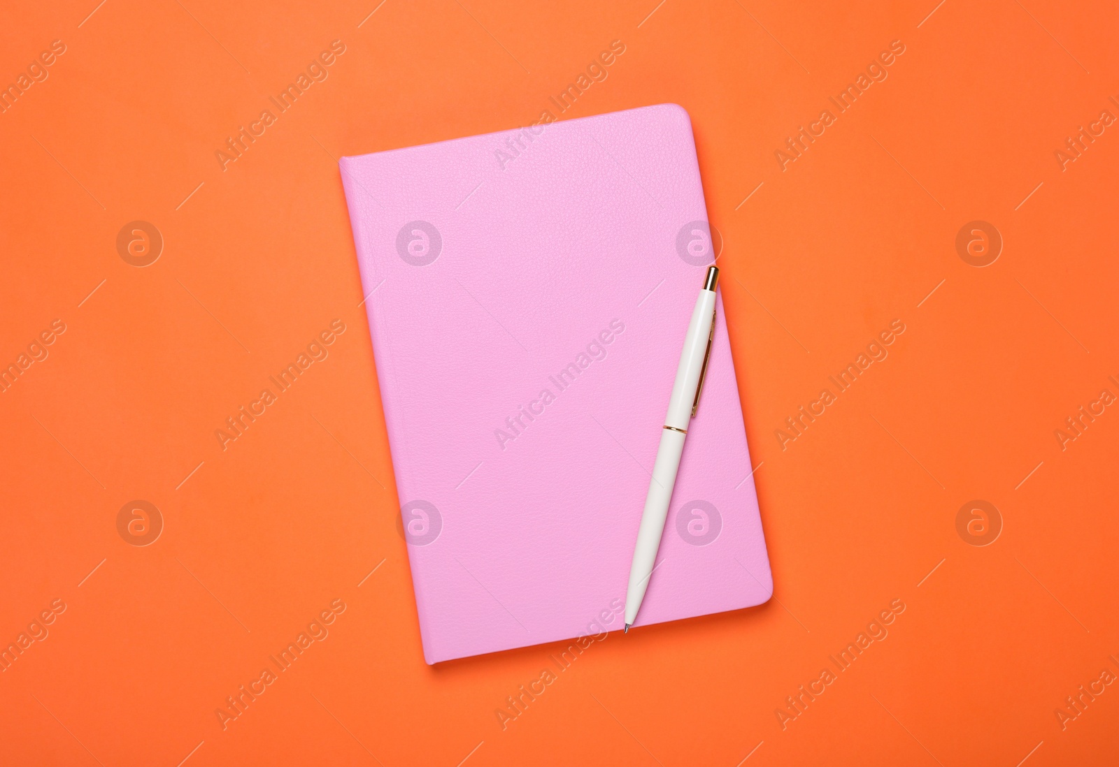 Photo of Closed pink notebook and pen on orange background, top view