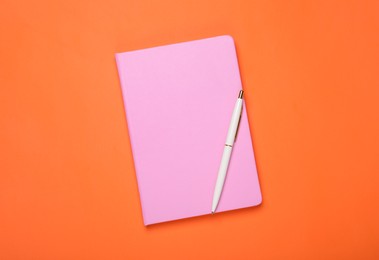 Photo of Closed pink notebook and pen on orange background, top view