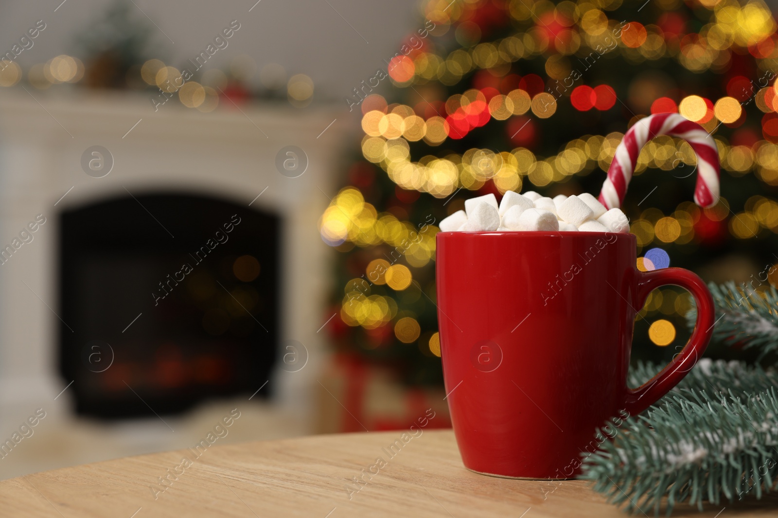 Photo of Christmas cocoa with marshmallows and candy cane in red cup on wooden table indoors, closeup. Space for text