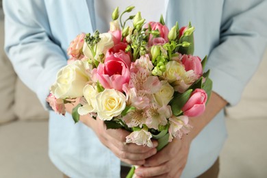 Photo of Man holding bouquet of beautiful flowers indoors, closeup